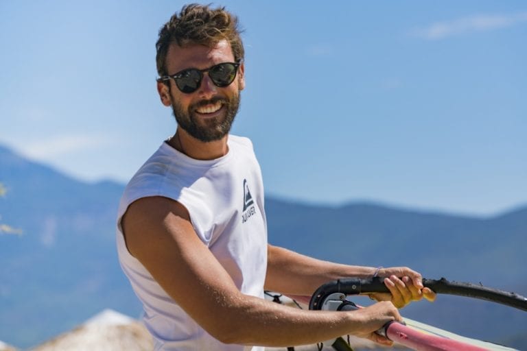 A man smiling while carrying a windsurf sail on the beach outside the Zefiros Beach Hotel in Samos, Greece