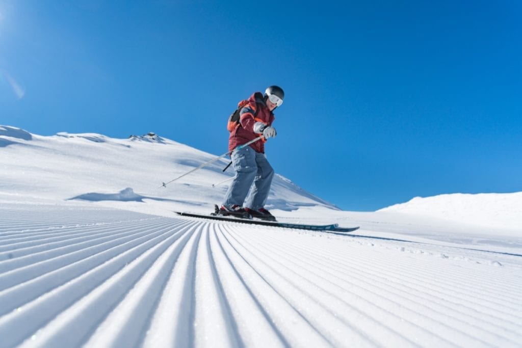 A man skiing on the freshly groomed piste with blue skies and snow