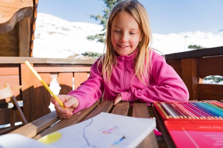 A young girl drawing a picture on the balcony while on a ski holiday