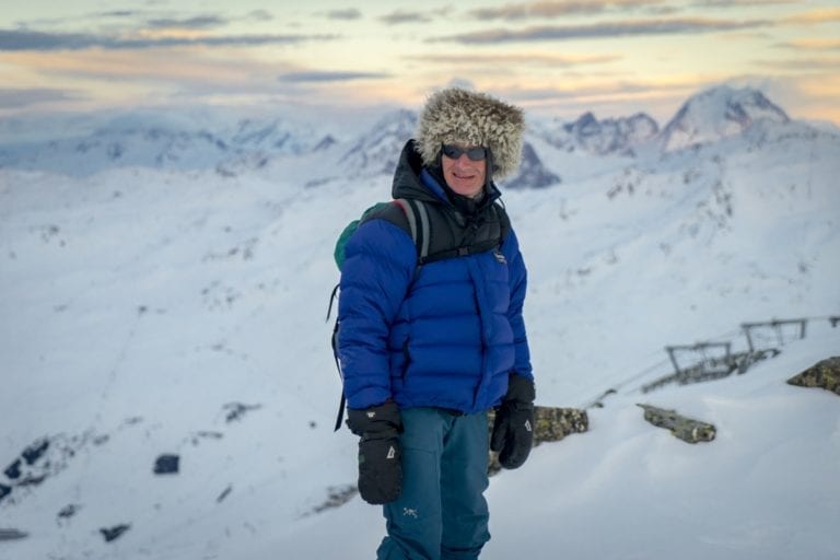 A man dressed for a ski holiday in the snow looking out over the mountains