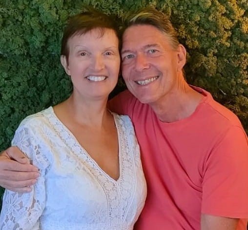 Phil and Sharon, ministry leaders, stood in front of a bush, smiling, Phil has his arm around Sharon