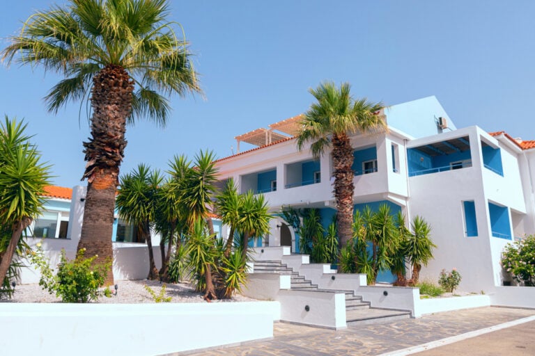 Side view of the front of the hotel. Palm trees on either side of the staircase that leads up to the hotel