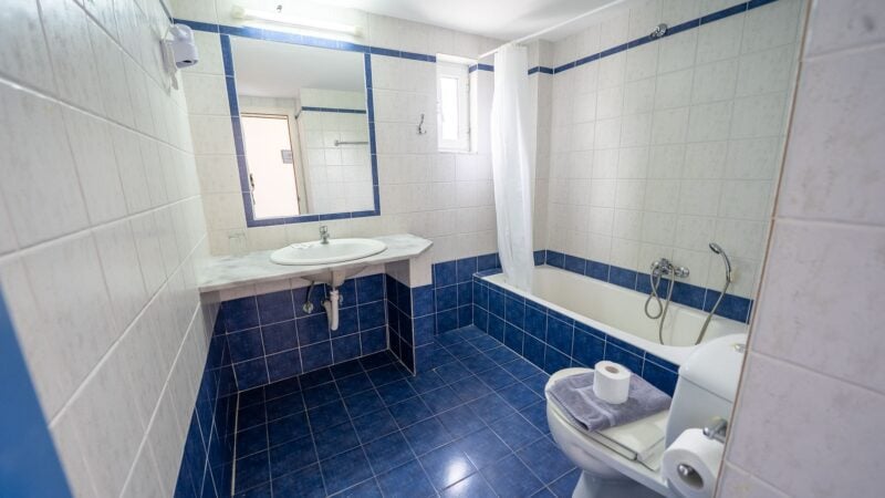 A white and blue tiled Upper-Level Room bathroom with sink, toilet and shower-over-bath.