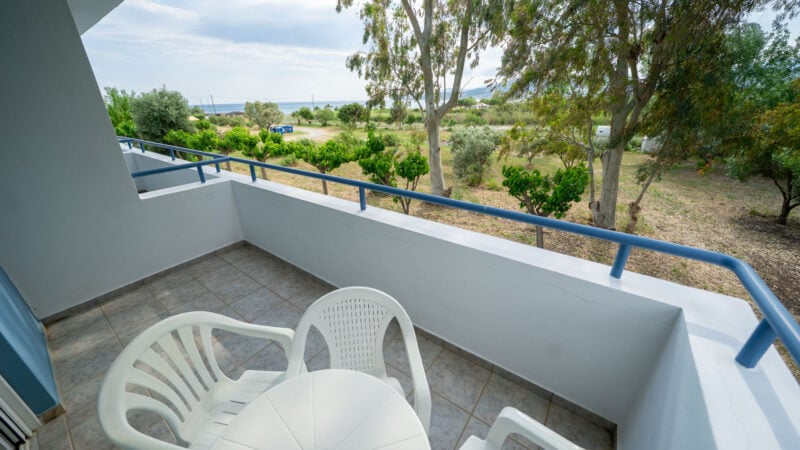 White plastic table and chairs on a hotel room balcony overlooking the beach and vegetation next to the hotel.