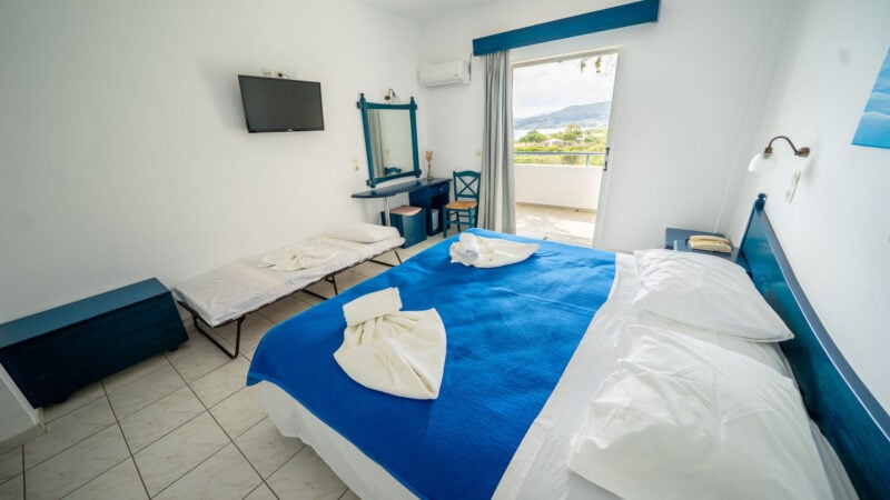 An Upper-Level Room with a mirror and flatscreen TV on the wall and two twin beds together to form a double bed with a blue blanket and towels on top.
