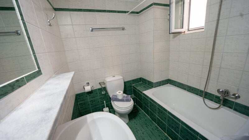 Lower-Level Room bathroom with sink, toilet and shower-over-bath on green tiling.