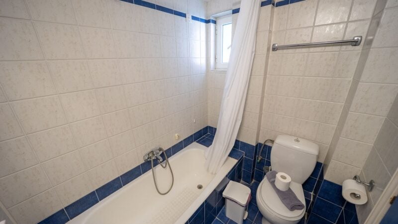 A white and blue tiled Upper-Level Room bathroom with sink, toilet and shower-over-bath.