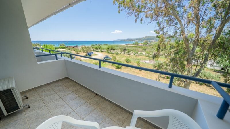 The balcony of an Upper-Level Room with white plastic table and chairs overlooking the sea