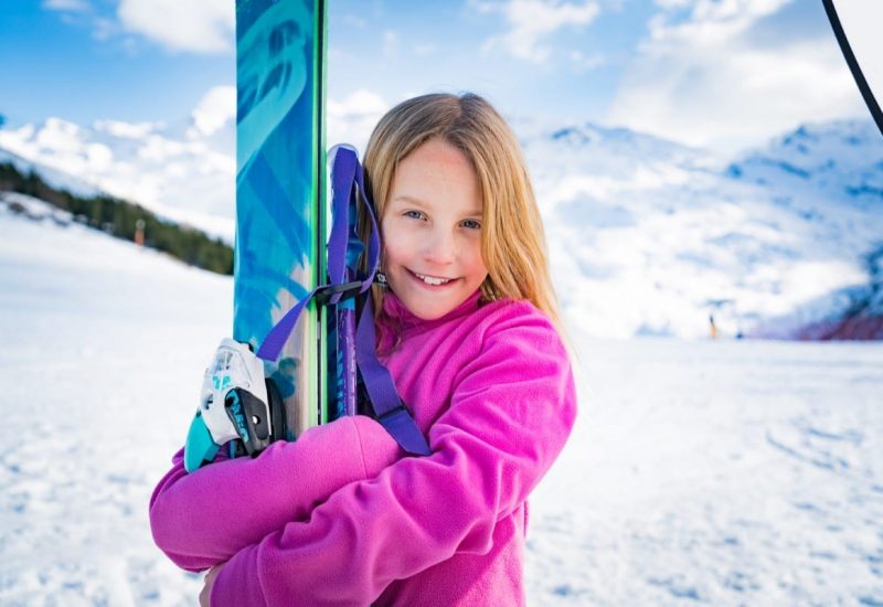 A young girl holding her skis and smiling while on holiday